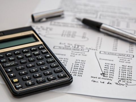 A black calculator and a sheet of white paper with financial statements on top of a white surface.