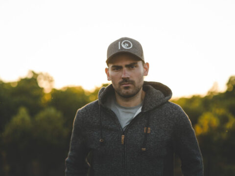 outdoor portrait of Tentree and Veritree CEO Derrick Emsley he wears a branded baseball hat and hoodie with out of focus forest in the background