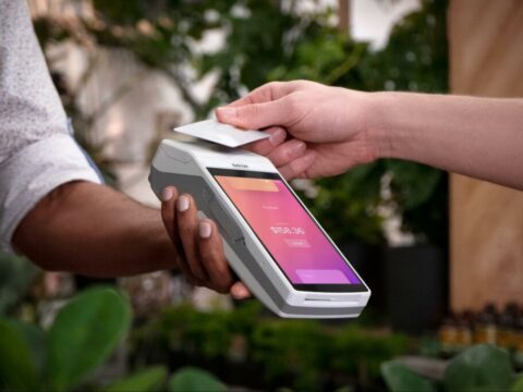 someone taps a payment card on a handheld terminal with a pink user interface on the screen