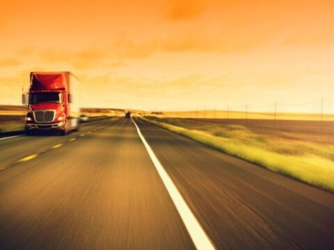 a red transport truck driving toward the camera with an orange tinted backdrop